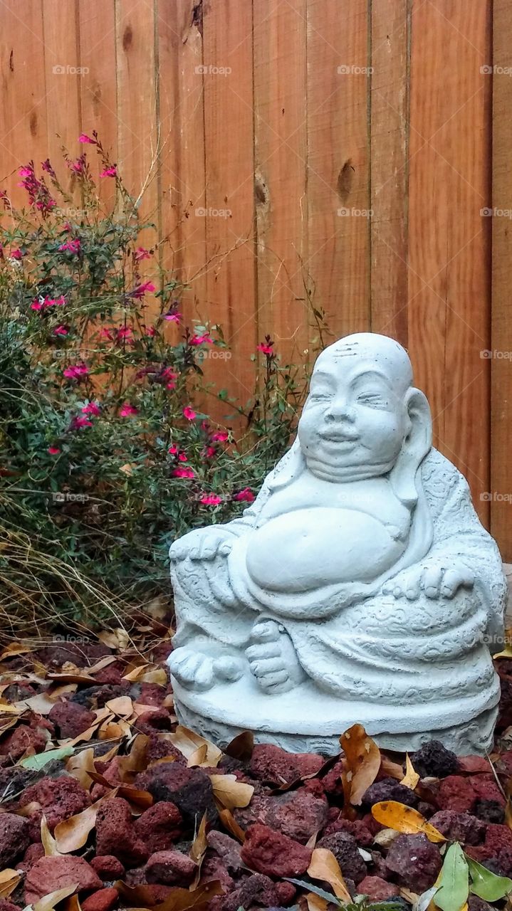 Happy grey buddah statue  offset by a striking display of pink salvia surrounded by fall colors