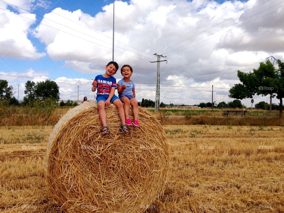 two children seated on a Bale of straw