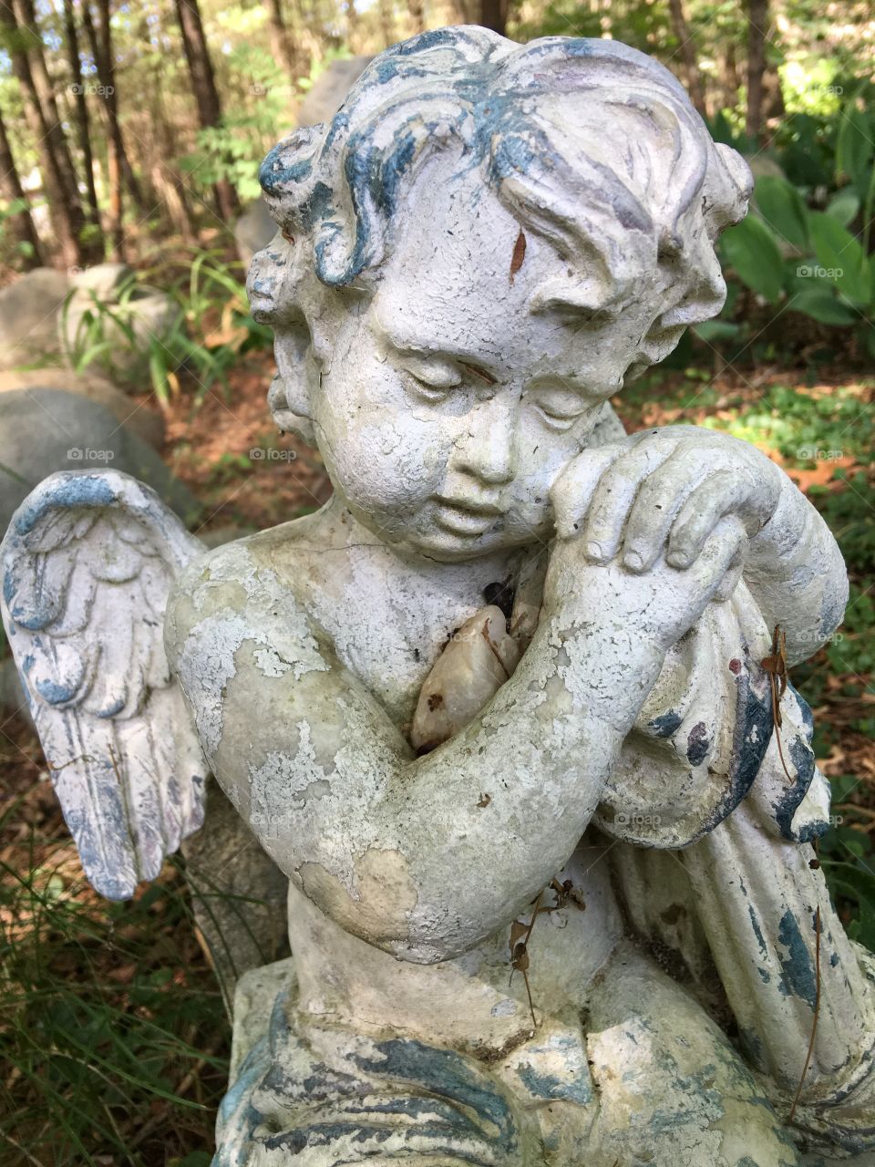 Angel sitting, aging, watching over place near woods.