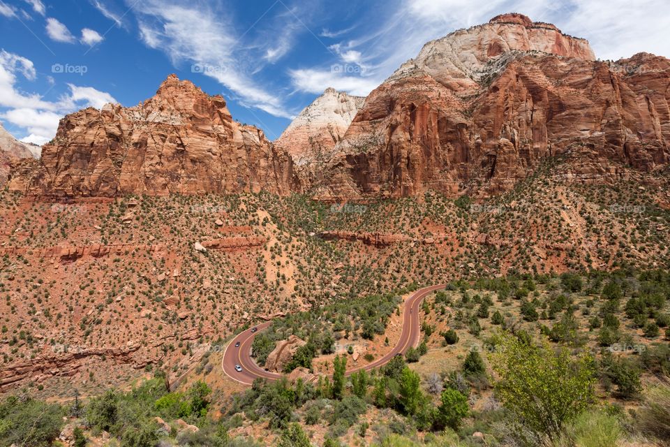 Hairpin road on mountains. Red, paved curvy road next to high red mountains. Few clouds. Road looks like question mark. Zion National Park, Utah