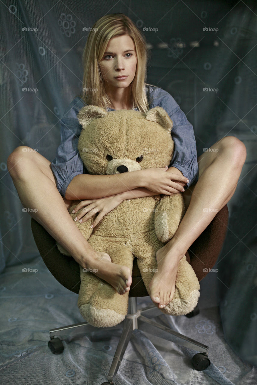 blonde girl with teddy bear. blond girl sitting on the chair with big teddy bear in her lap
