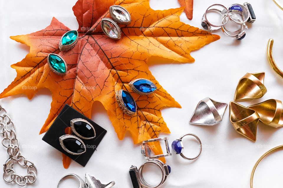 Earrings and necklaces. Beautiful lady accessories of colorful earrings and necklaces on display. Top view. Maple leaf as display background