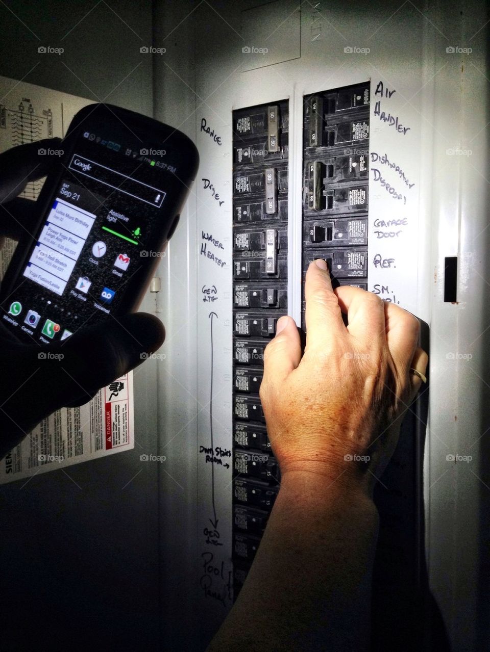 Man using smart phone as flashlight to check breakers in the house