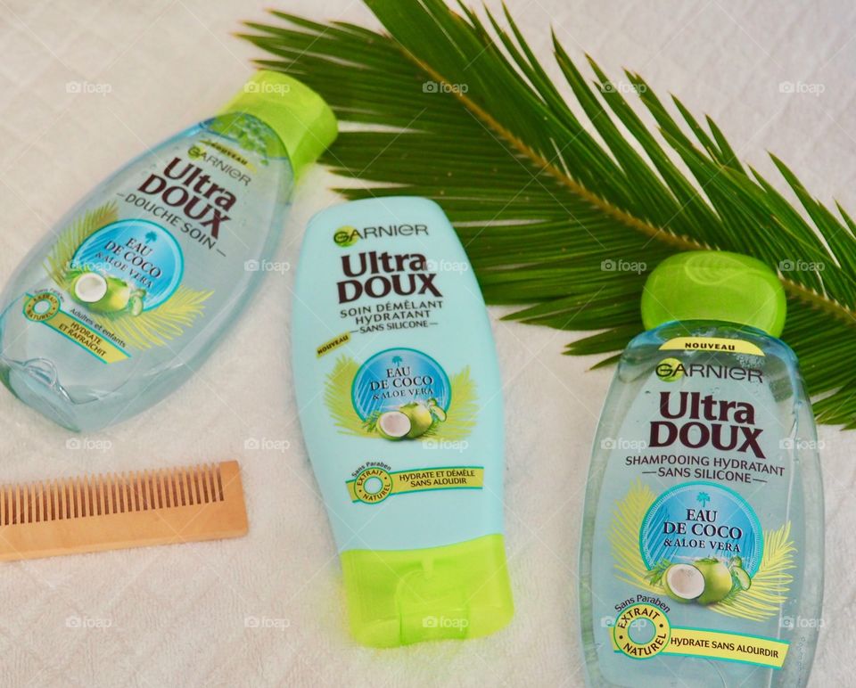 Garnier eau de coco shampoo, conditioner and bath gel on white towel with comb and palm branch.