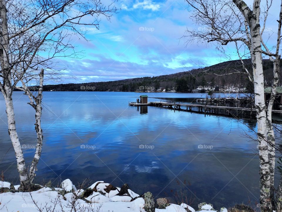 A winter scene in New Hampshire of a beautiful lake, wintry blue skies and snowy bank is a perfect scene of nature at its best
