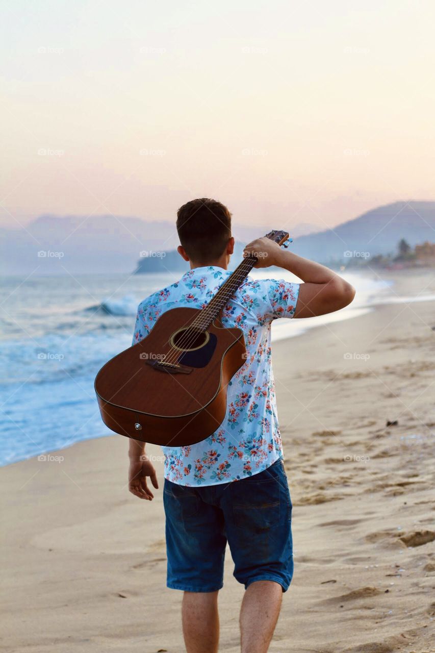 A boy watching the sunset with his guitar