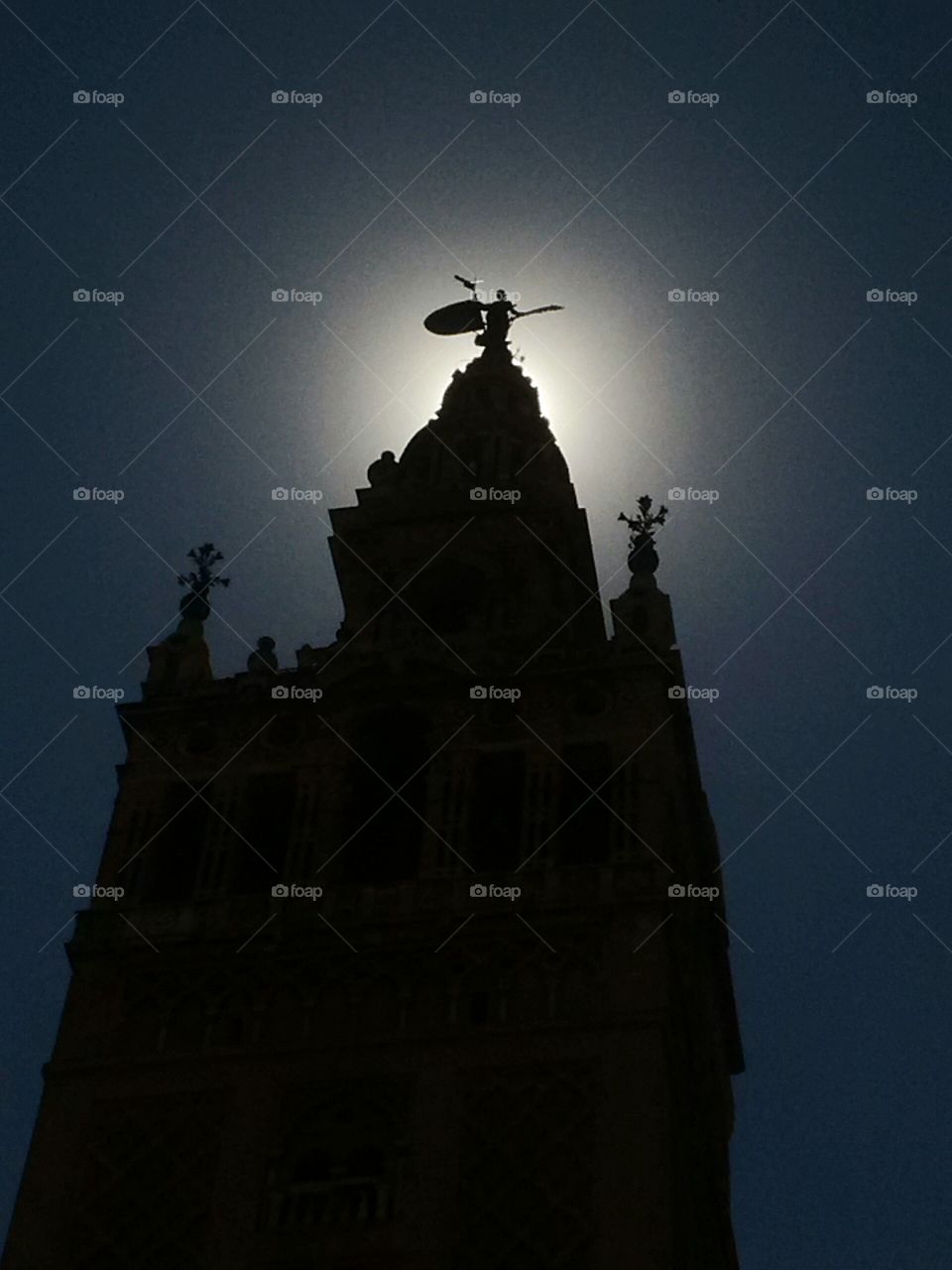 sun behind the very top of the Giralda tower, Seville, Spain.