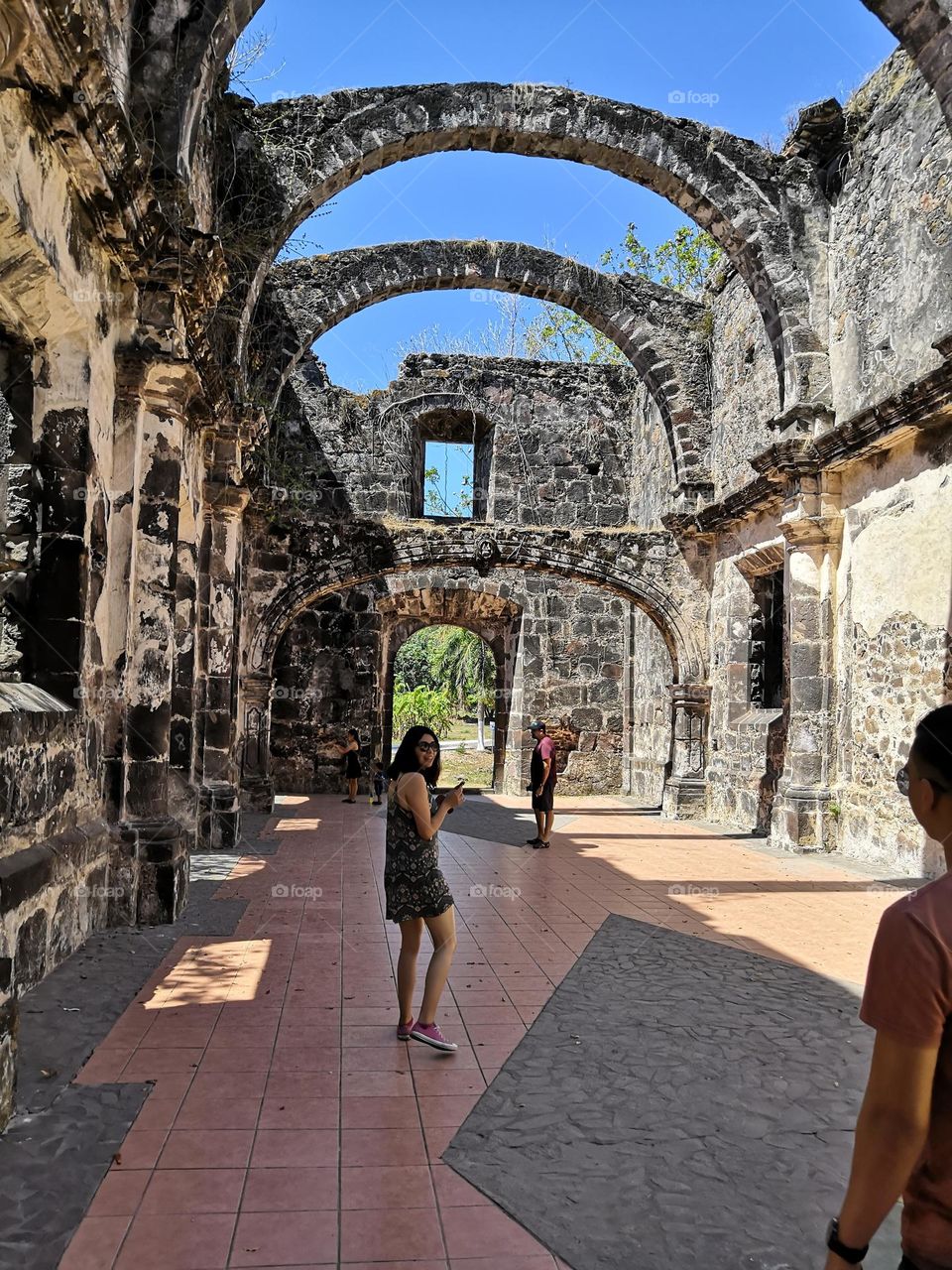 Tourists walking inside of an ancient temple ruins with large arches above with the sky as background.