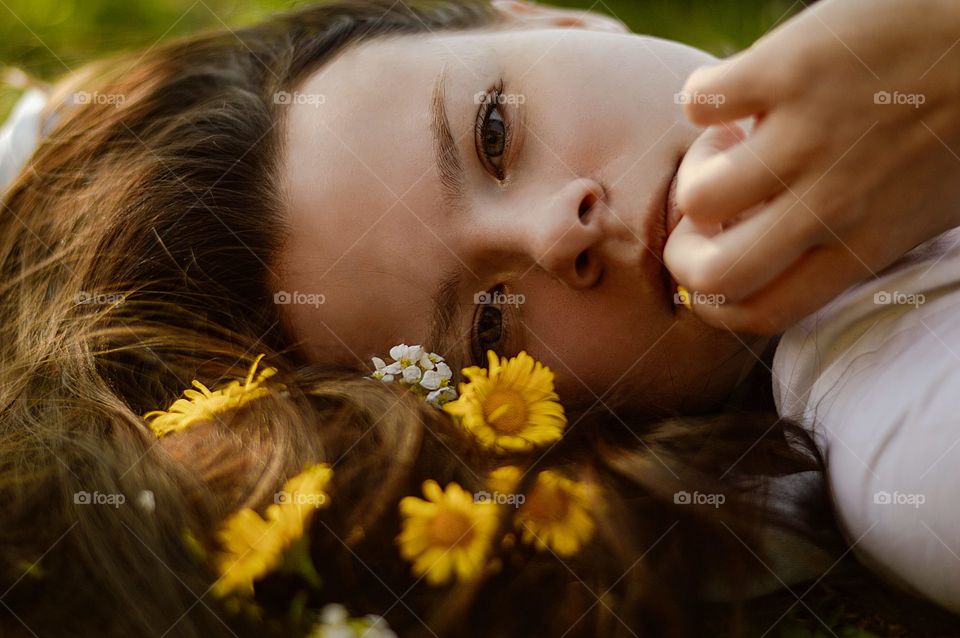 Girl lying on the ground with flowers in her hair. Looking derectly at the camera