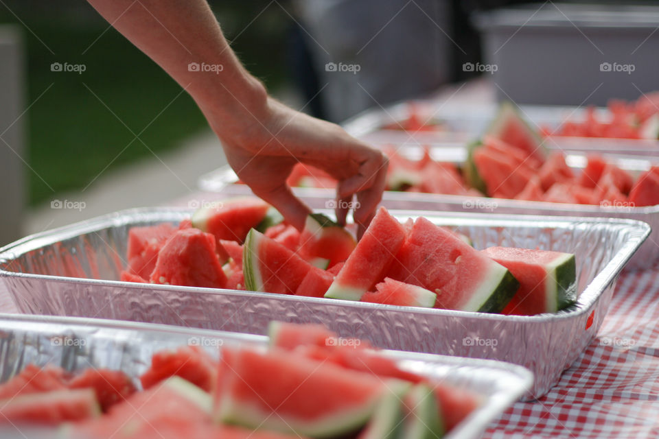 A hand reaches for a piece of fresh watermelon at an outdoor summer picnic