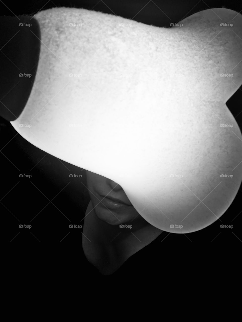 There is a lighted lamp. Behind the lamp is my head but only the mouth and part of the nose come out. The photograph is made with the iphone. The lamp is shaped like a flower.