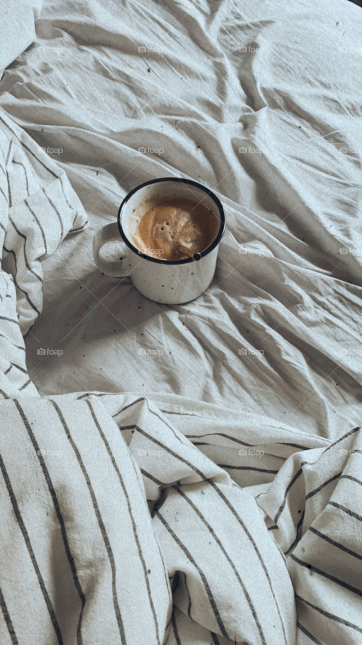 A cup of coffee sits on a bed with strong morning feelings.