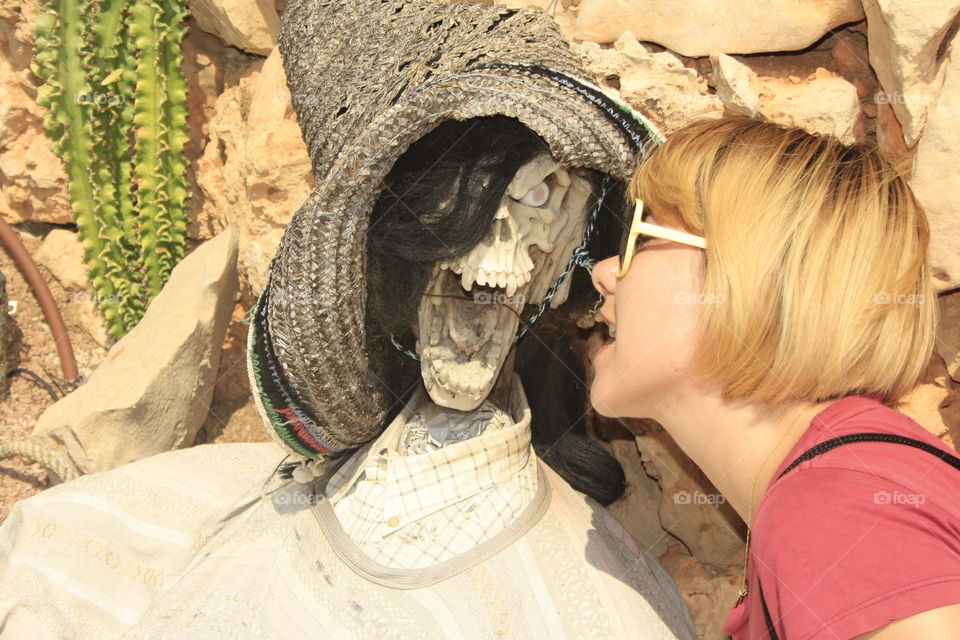 A funny photograph. It is a skeleton. I pretend to give the skeleton a kiss. The background is light brown.