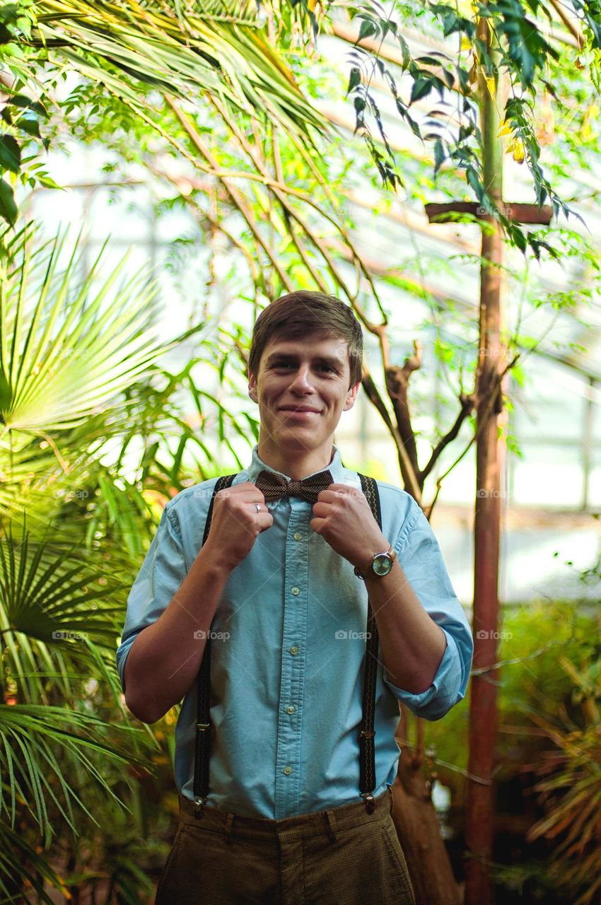 Lifestyle portrait of young, nice, cute,  handsome,  happy,  smiling man in casual clothes in greenhouse. Celebrating birthday.