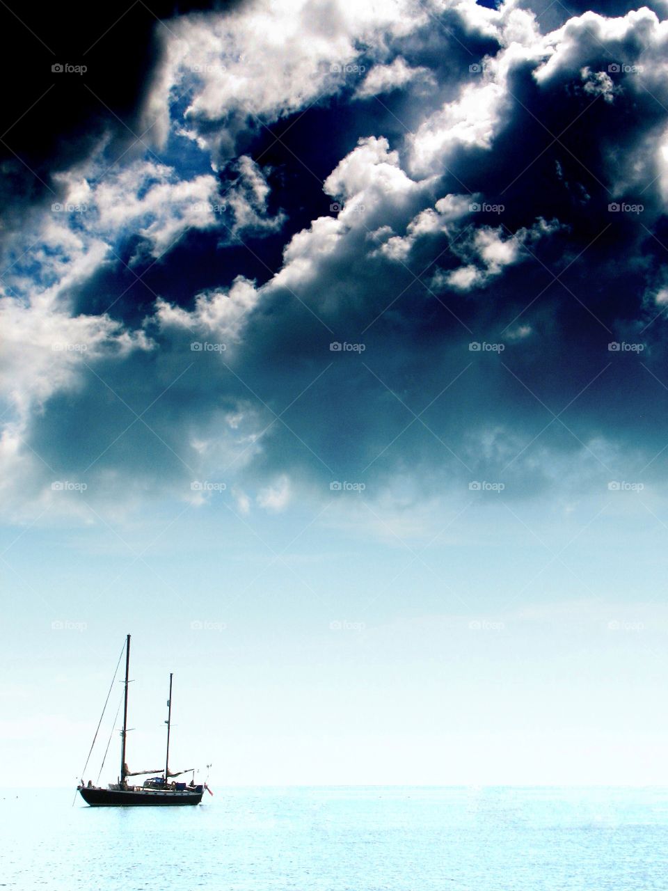 A lone boat floating on a calm Ocean with a dark, threatening cloud building overhead.