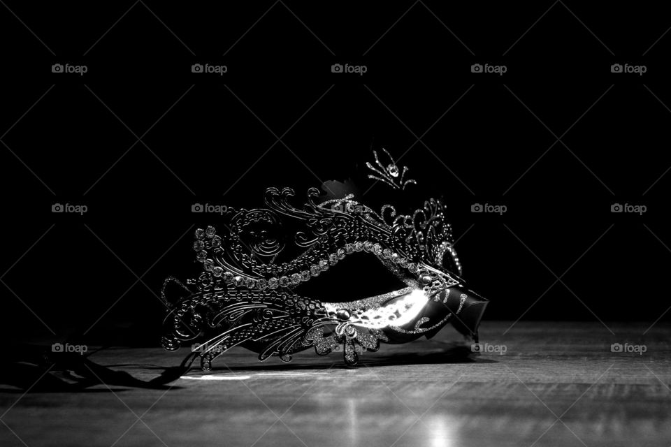 A black and white portrait of a venetian mask on a wooden table. It really is very mysterious in this darkness.