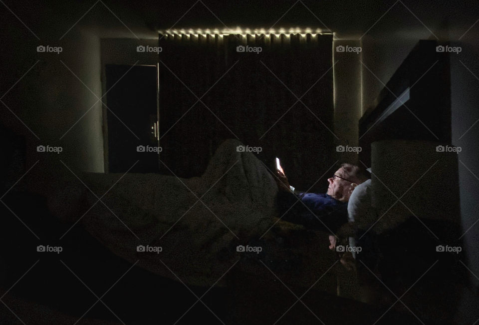 Man reading an ebook in a darkened bedroom 