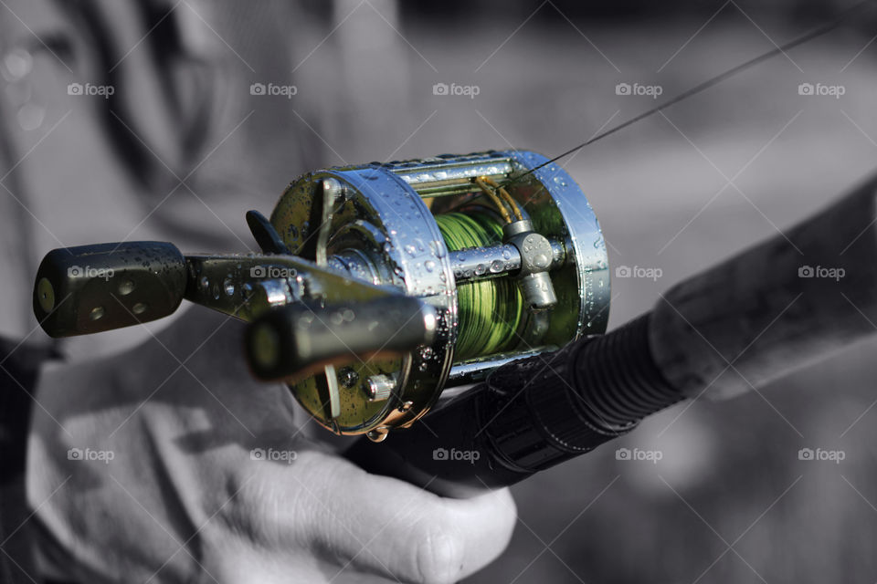 Male hand on a spool of a round fishing with selective colour processing