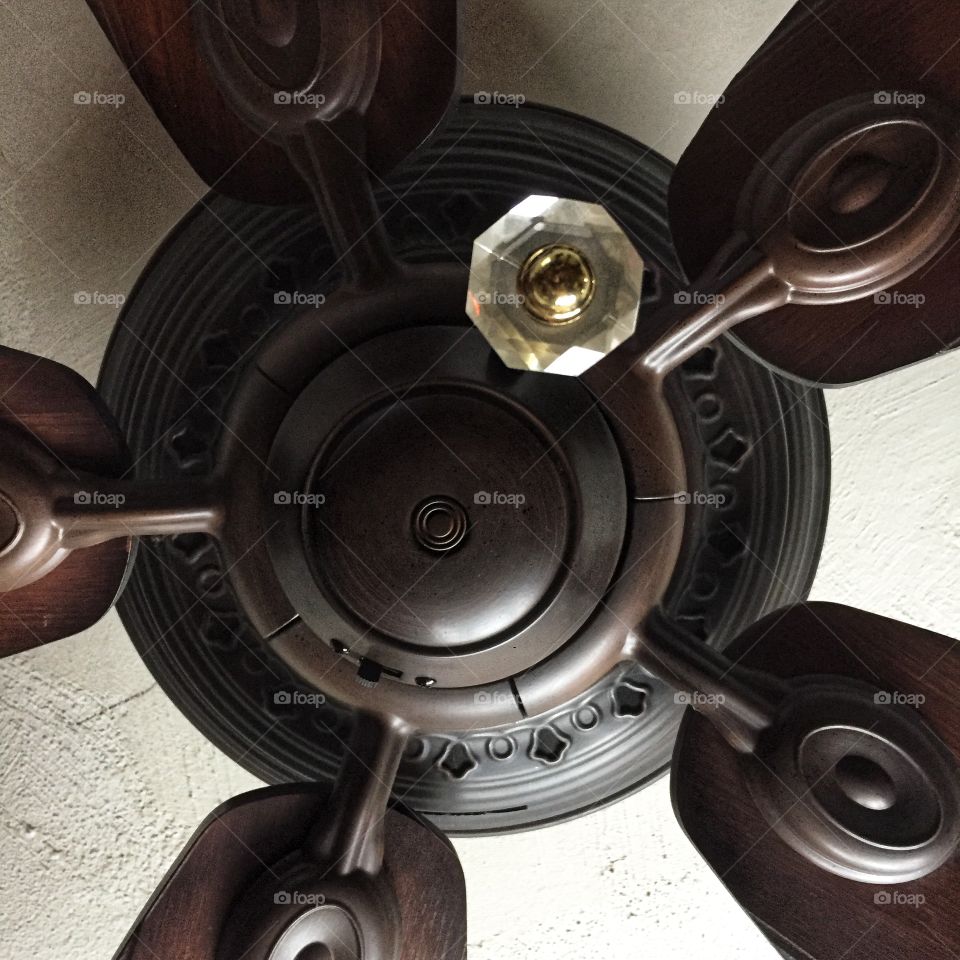 A black ceiling fan as seen from directly below. The round glass pull chain dangles down. The ceiling above is white.
