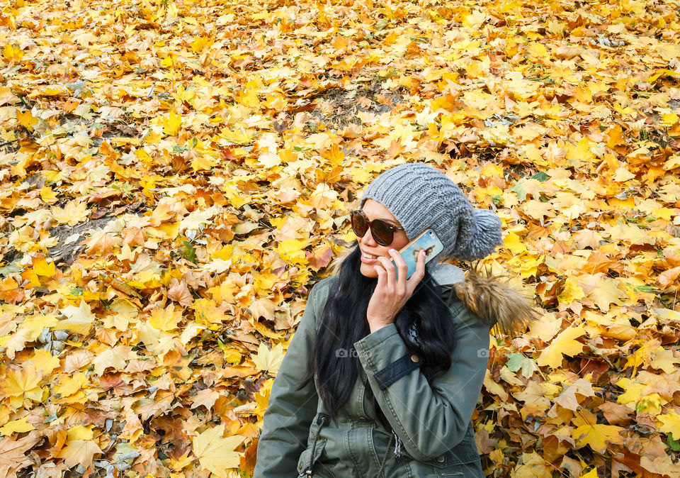 Young woman sitting on autumn leaves with mobile phone