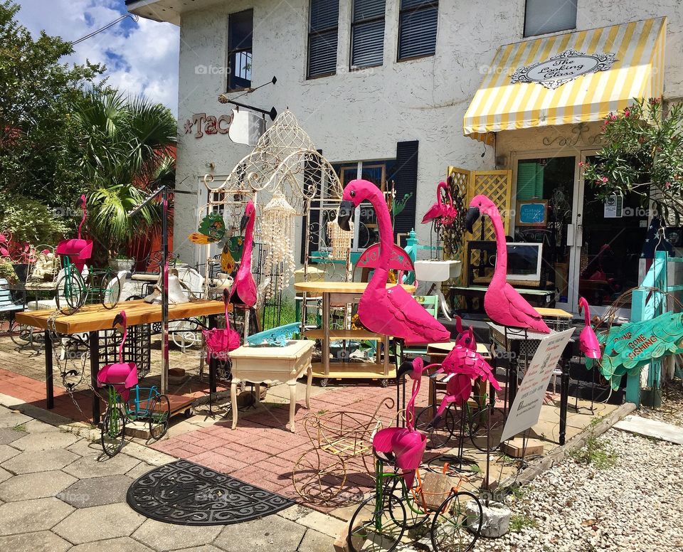 Giant pink flamingo statues, yard ornaments and flea market finds in display outside of a shop.