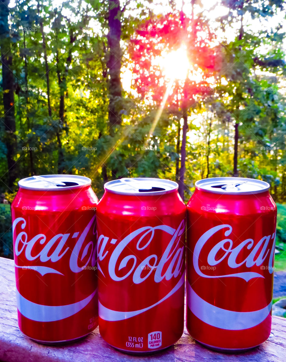 Cans of Coca Cola on a porch railing with the sun going down.