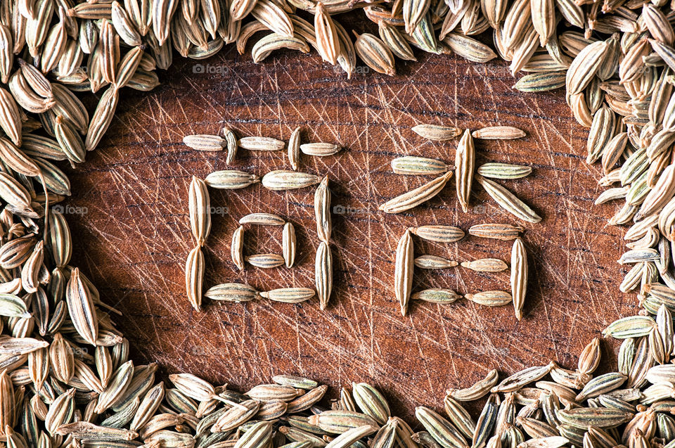 Word fennel written in Chinese characters using fennel seeds on wooden cutting board close up