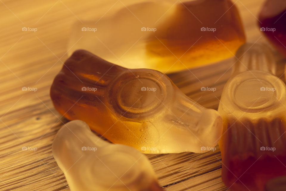 A macro close up portrait of pieces of candy shaped like cola bottles on a wooden table.