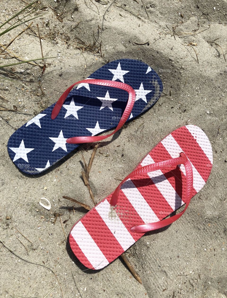 Red white and blue flip-flops are sitting in the sand.