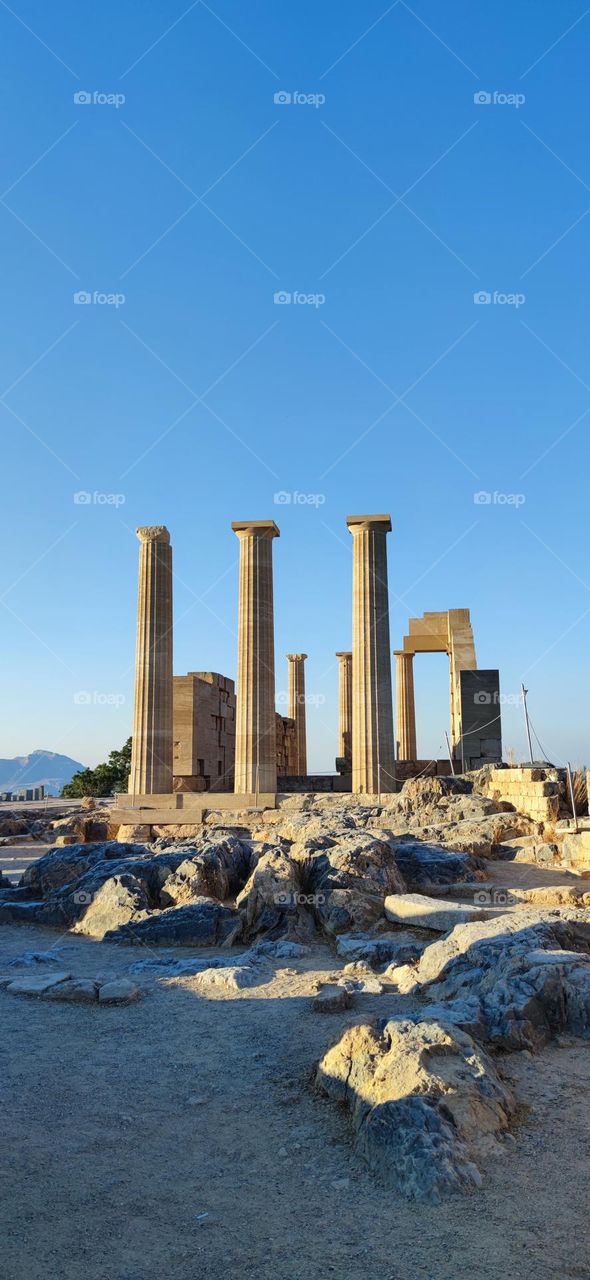 The remains of a ruined ancient temple to the goddess Athena with columns and an arch on a high mountain in the ancient city of Lindos, in Greece on the island of Rhodes, side view close-up. Concept ruined ancient acropolis of Lindos.