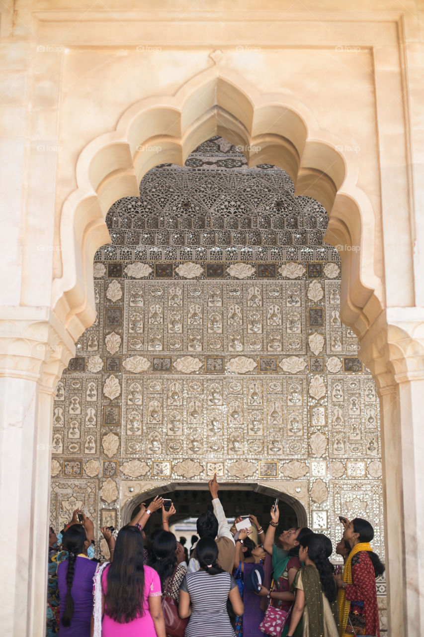 A group of women on a guided tour in India altogether look at the details of a ceiling and admire it. 