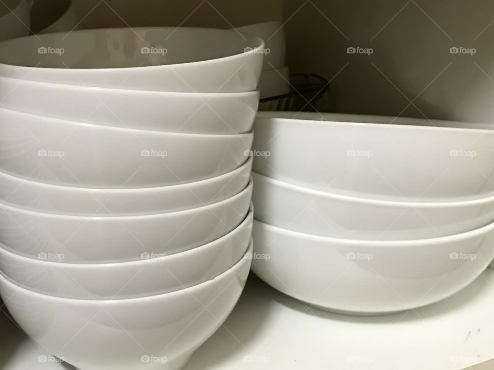 White ceramic bowls dishes stacked on white shelf, conceptual meal service or food preparation, commercial or home dishes, repetitive, home kitchen organisation