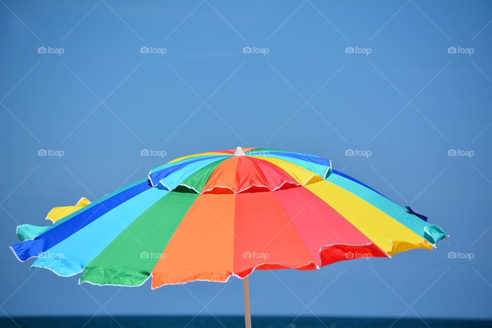 Bright rainbow colored beach umbrella against a clear blue sky