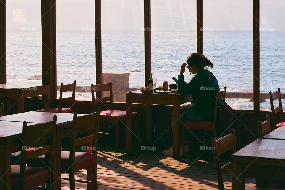 Lonely girl sitting at the table next to window in a restaurant 