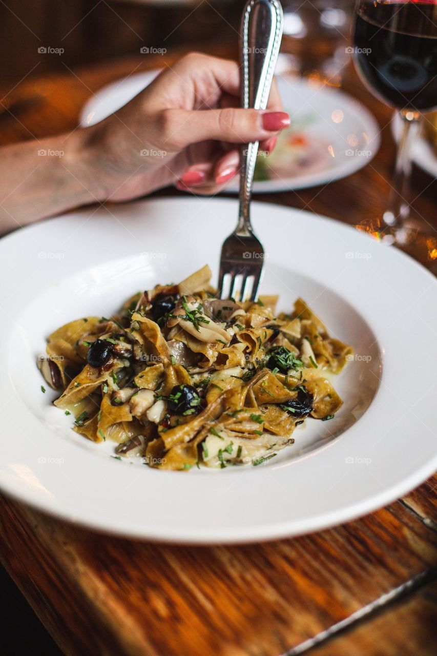 A clean white bowl is stuffed with gourmet pasta  with mushrooms and your fork is inserted into the first bite of this tempting dish.