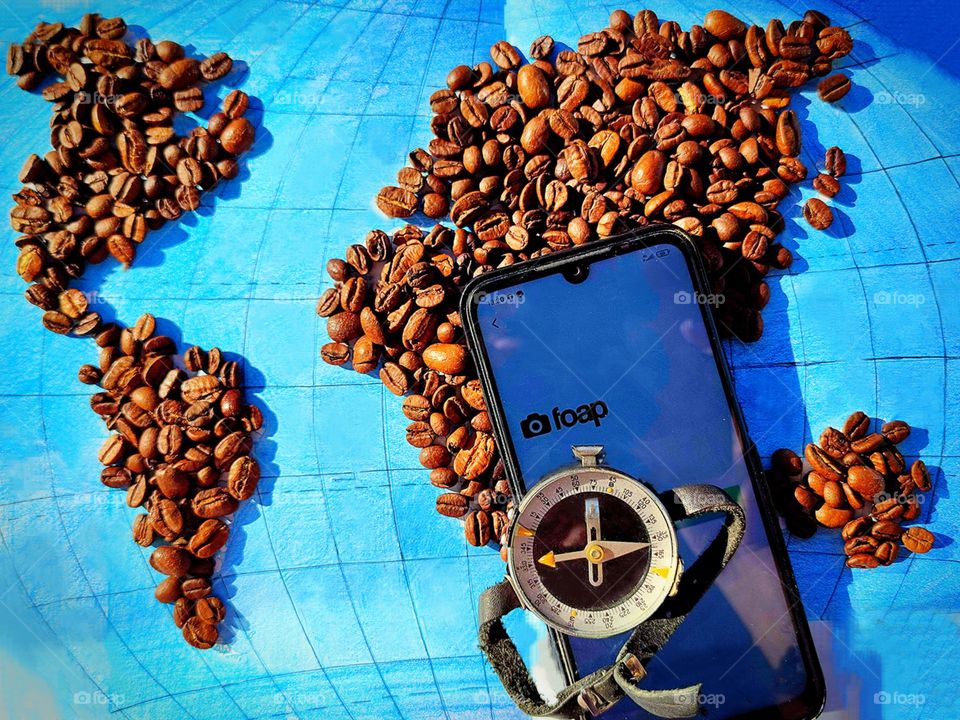 On the world map, large continents are laid out with black coffee beans: North America, South America, Africa, Eurasia and Australia. On the map is a cell phone with an open page "Foap" and a compass