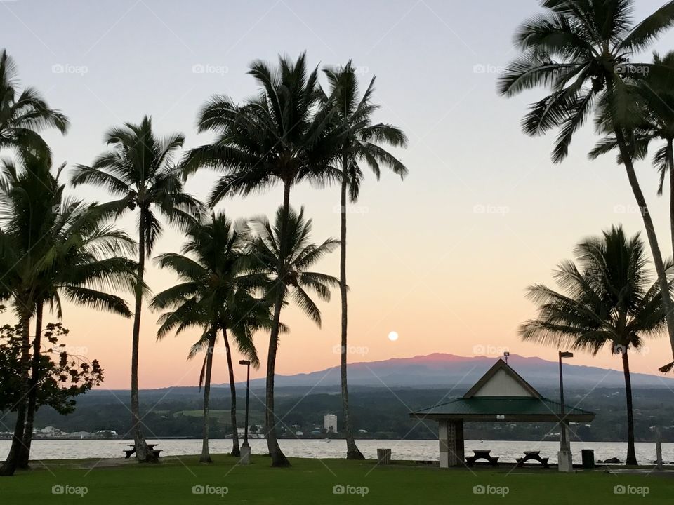 Moon receding as the sun illuminates the volcano