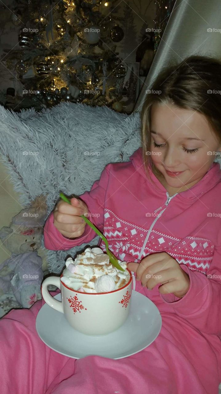 a little girl on Christmas eve enjoying a extra large hot chocolate with cream and marshmallows.