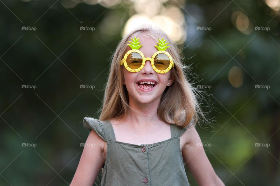 Candid portrait of happy little Caucasian girl with blonde hair wearing stylish sunglasses 