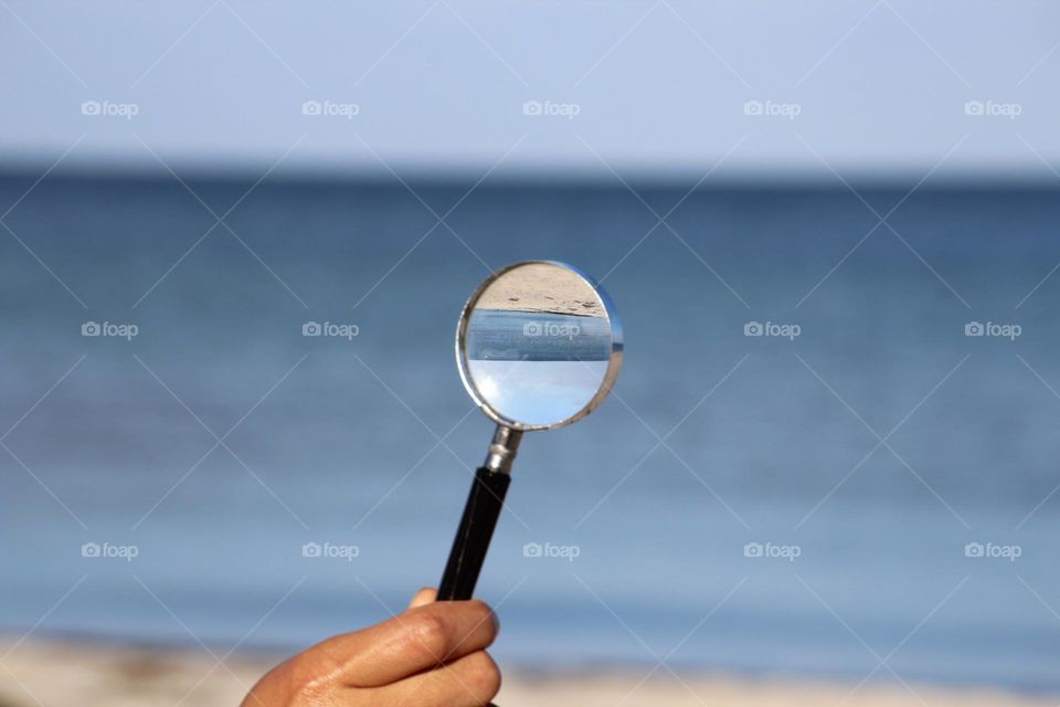 Hand with a magnifying glass at the beach mirroring the beach upside down.