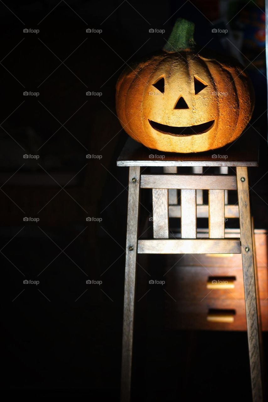 An orange decorative pumpkin stands on a brown wooden shelf and is illuminated by the sun