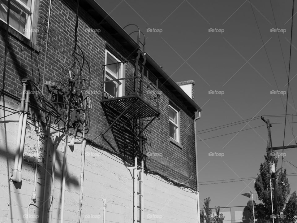 The side of an old concrete building in a city with windows and a fire escape ladder on a sunny summer day. 