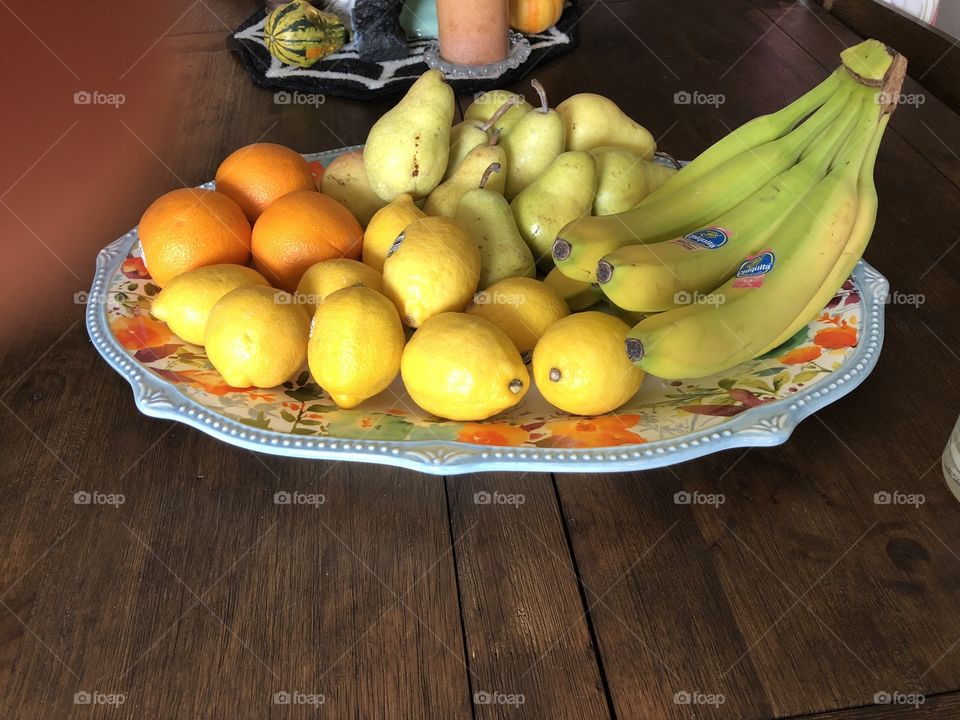 Large pioneer woman platter full of lemons, oranges, pears and bananas on a dark wood table. 