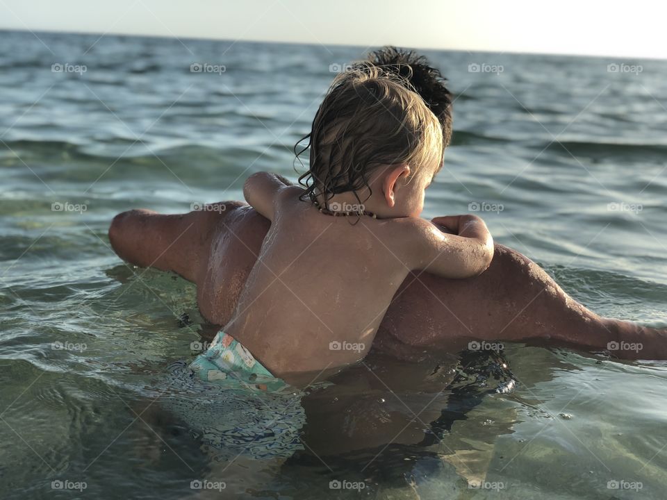 Father and son floating in the ocean, waiting for sunset. Summer nights. 