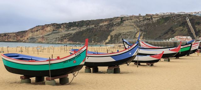 Brightly coloured, wooden fishing boats sit on the sand at Praia Da Nazaré, Portugal 