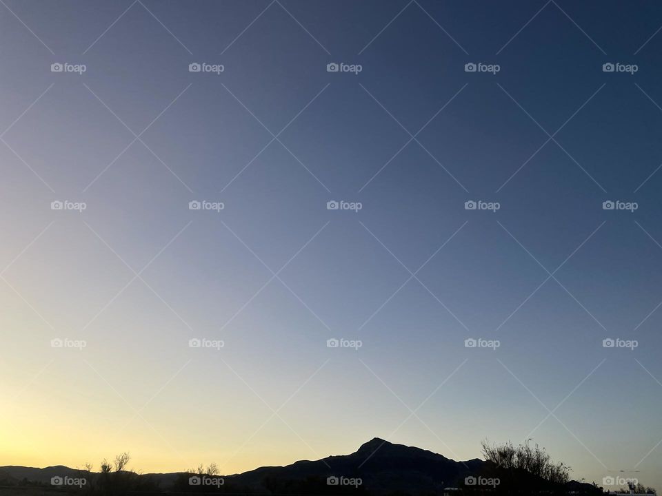 A yellow and blue sunset with mountains and tree branches.