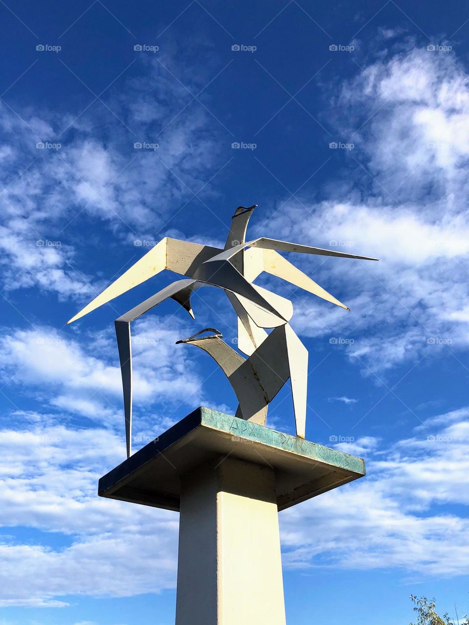 Abstract sculpture: two metal seagulls on the pedestal against deep blue sky with white clouds