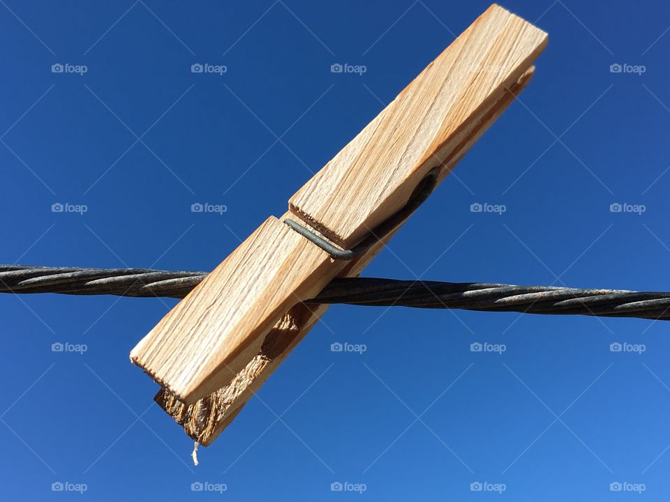 Single wood clothespin on a wire clothesline against the vivid blue sky