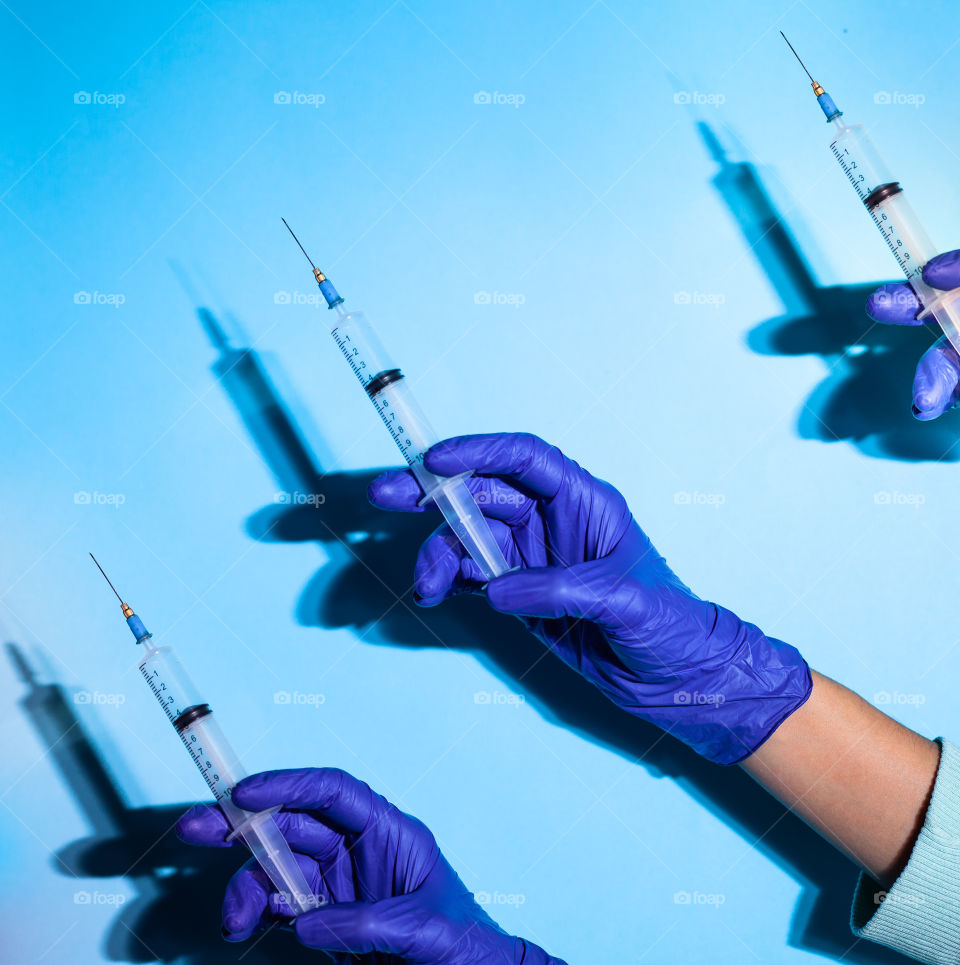 A hand in a blue glove holds a syringe. Medical background. The doctor holds a syringe for vaccination. Medicine. Blue background, place for text. Copy space.	