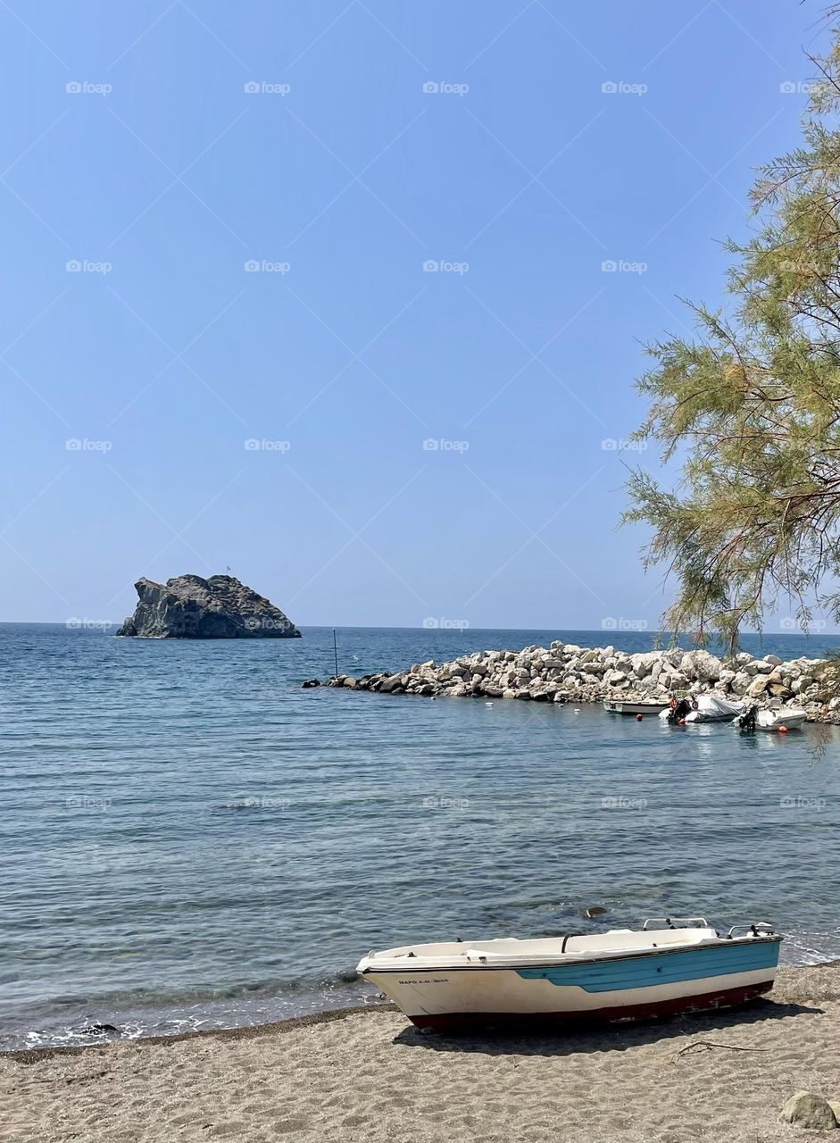 Fishing boat on the beach in Skala Eressos harbor on the sunny Greek island of Lesbos with view of the rock